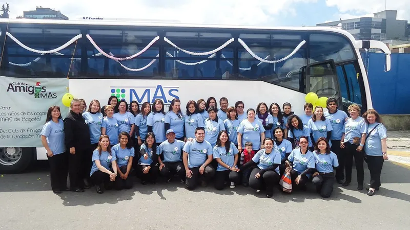 Integrantes del Club de Amigos MAS con camisetas azules frente a un bus de la fundación