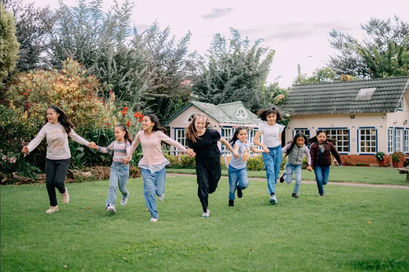 Grupo de niñas corriendo tomadas de la mano por el césped de un jardín