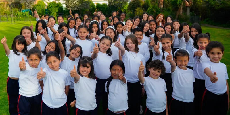 Grupo grande de niñas y niños con camiseta blanca haciendo el gesto de pulgar arriba en un jardín