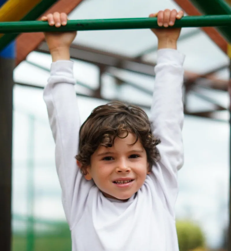 Niño sonriente colgado de una barra en un parque infantil