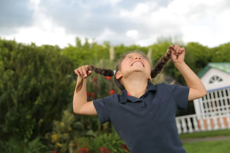Niña feliz jugando con sus trenzas en el jardín del albergue