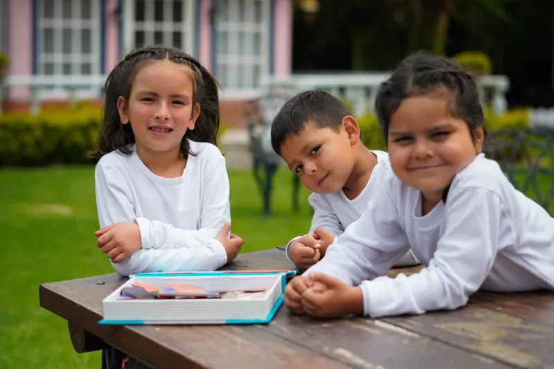 Tres niños sonrientes apoyados en una mesa de madera en el jardín